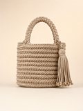 Beige handvirkad Bucket-väska med flätat handtag och lång tofs på varm studiobakgrund.